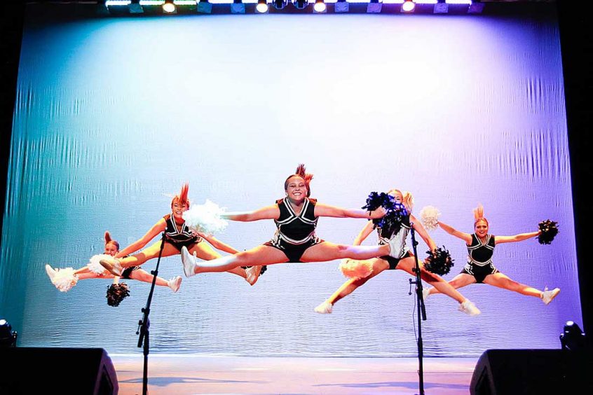 Cheerleaders jumping during a dance with pom poms